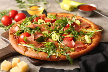 Wooden board of delicious pizza with tomatoes and arugula on grey background