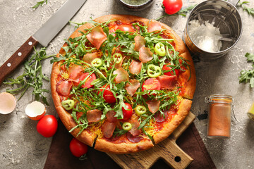 Wooden board of delicious pizza with tomatoes and arugula on grey background