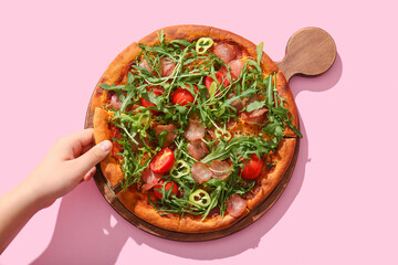 Woman taking piece of delicious pizza with tomato and arugula on pink background