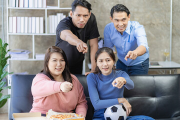 Young Asian men sitting on the sofa watching and cheering on football or football match on TV together at home and celebrating the victory.