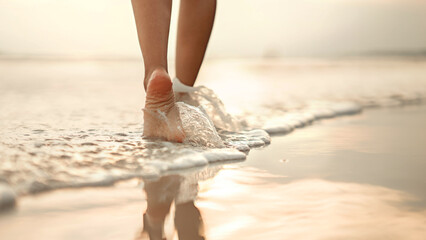 Closeup of woman feet walking on sand beach during a golden hour sunset. Travel and relaxing in...