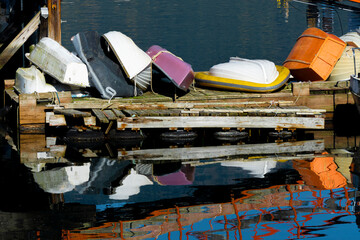 An image of several small row boats and fishing boats stacked on a wooden pier creating a colorful...