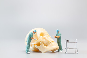 Miniature people Doctor with a giant human skull on a grey background