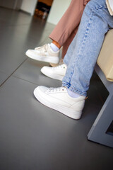 Female legs in white sneakers and jeans
