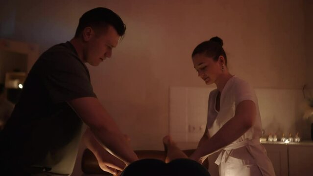 Massage therapists do a synchronous massage under candlelight. Massage parlor. A man and a girl in medical gowns.
