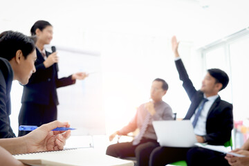 Businesswoman hand holding a pen ready for taking note at the meeting with blurred background of businesspeople group at conference. Secretary officer taking minutes for making a report.
