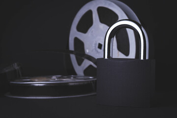Movie screening ban. Forbidden film. Indoor cinema.Film reel and padlock on a black background.