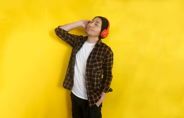 Emotional Asian man with headphones enjoy listening music on yellow background