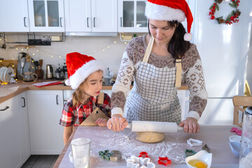 Mom and daughter in the white kitchen are preparing cookies for Christmas and new year. Family day, preparation for the holiday, learn to cook delicious pastries, cut shapes out of dough with molds