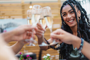 A radiant woman with braided hair toasting with champagne glasses among friends at an outdoor...