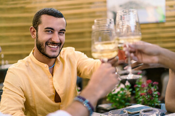 A smiling man in a yellow shirt toasting with white wine, enjoying a convivial moment with friends - enjoyable wine tasting event, Friendly toast with white wine