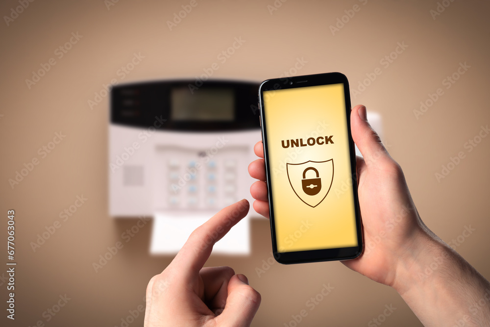 Poster man operating home alarm system via mobile phone against beige wall with security control panel, clo