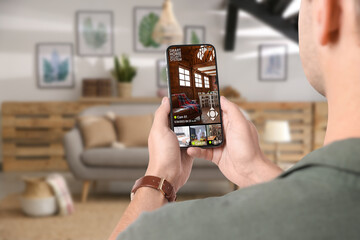 Man using smart home security system on mobile phone indoors, closeup. Device showing different...