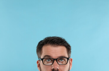 Man in stylish glasses on light blue background, closeup