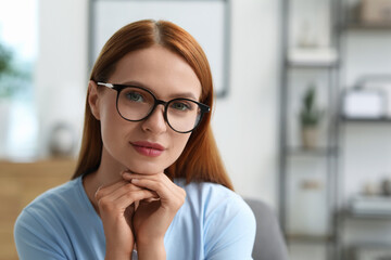 Portrait of beautiful young woman with red hair at home. Attractive lady in glasses looking into camera. Space for text