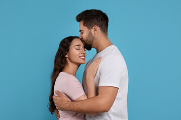 Man kissing his smiling girlfriend on light blue background