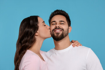 Obraz premium Woman kissing her smiling boyfriend on light blue background