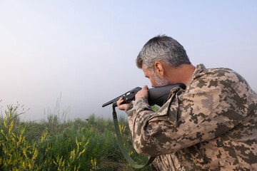 Man wearing camouflage and aiming with hunting rifle outdoors. Space for text
