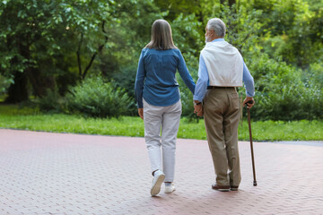 Senior man with walking cane and mature woman outdoors, back view. Space for text