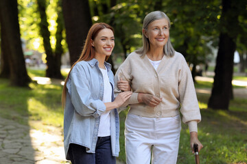 Senior lady with walking cane and young woman in park