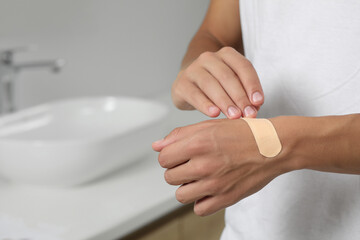 Man putting sticking plaster onto hand indoors, closeup. Space for text