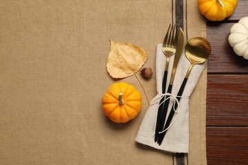 Cutlery, napkin and pumpkins on brown tablecloth, flat lay with space for text. Table setting