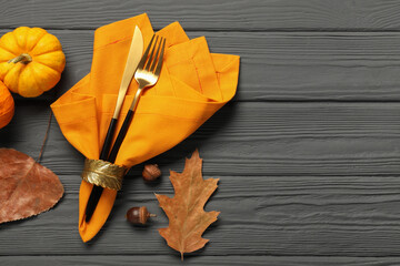 Cutlery, napkin and autumn decoration on gray wooden background, flat lay with space for text....