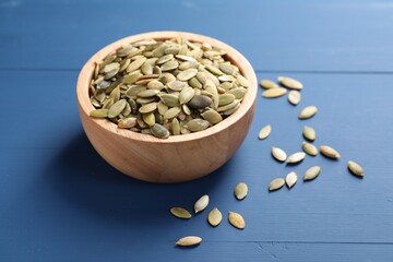 Bowl with peeled pumpkin seeds on blue wooden table
