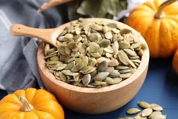 Bowl with seeds, spoon and fresh pumpkins on blue wooden table, closeup