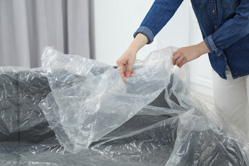Woman putting plastic film away from sofa at home, closeup