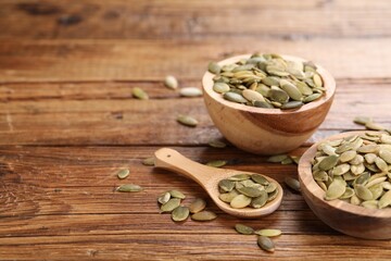 Bowls and spoon with peeled pumpkin seeds on wooden table. Space for text
