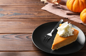 Piece of delicious pumpkin pie with whipped cream and fork on wooden table, space for text