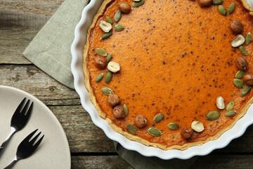 Delicious pumpkin pie with seeds and hazelnuts served on wooden table, flat lay