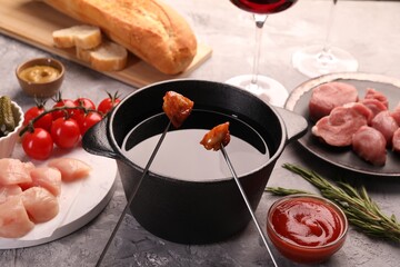 Fondue pot, forks with fried meat pieces and other products on grey textured table