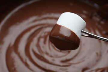 Marshmallow with melted chocolate on fork above fondue, closeup. Space for text