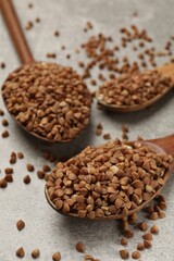 Spoons with dry buckwheat on grey table, closeup