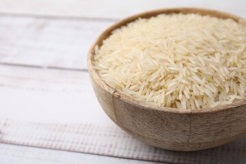 Raw rice in bowl on light wooden table, closeup. Space for text