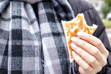 .Hands with white nails and a bite of breakfast bread on a background of a gray checkered scarf