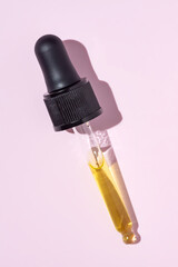Bottle pipette dropper and Liquid yellow-orange retinol or vitamin c gel or serum on pink background