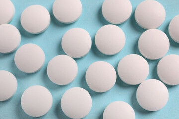 Many white pills on light blue background, flat lay