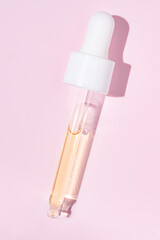 close up of pipette with pouring liquid serum and shadows on pink background. Trendy cosmetics shot with hard shadows.