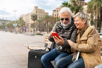 Active senior couple tourists traveling together using cell phone to check hotel restaurant...