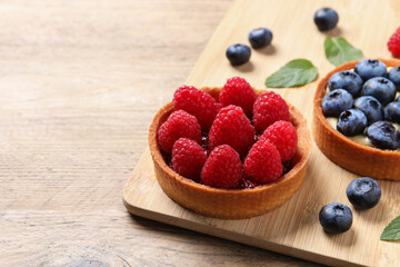 Tartlets with different fresh berries on wooden table, space for text. Delicious dessert