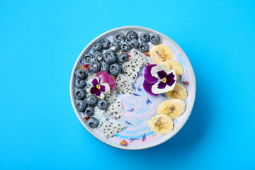 Obraz na płótnie Canvas Delicious smoothie bowl with fresh fruits, blueberries and flowers on light blue background, top view