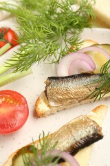 Delicious sandwiches with sprats, pickled cucumber, onion and dill served on plate, closeup