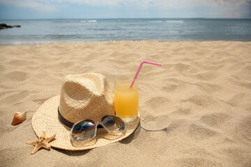 Fototapeta na wymiar Straw hat, sunglasses and refreshing drink on sandy beach near sea. Space for text
