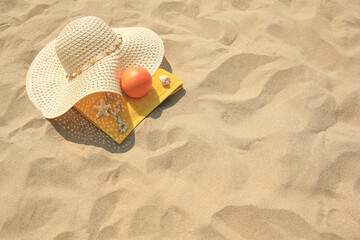 Fototapeta na wymiar Straw hat, towel and orange on sand, above view. Space for text