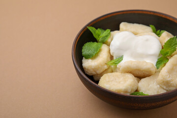 Bowl of tasty lazy dumplings with sour cream and mint leaves on light brown background. Space for...
