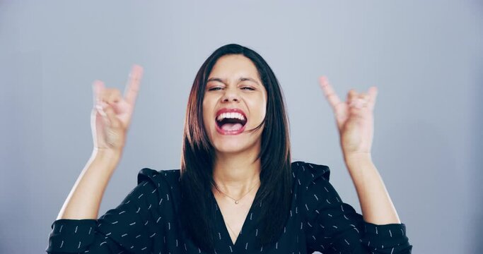 Face, rock and roll with woman, hand and happiness with an attitude on a grey studio background. Portrait, person and model with emoji, symbol or heavy metal music with a smile, energy and culture