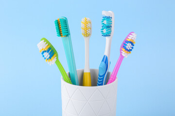 Different toothbrushes in holder on light blue background, closeup